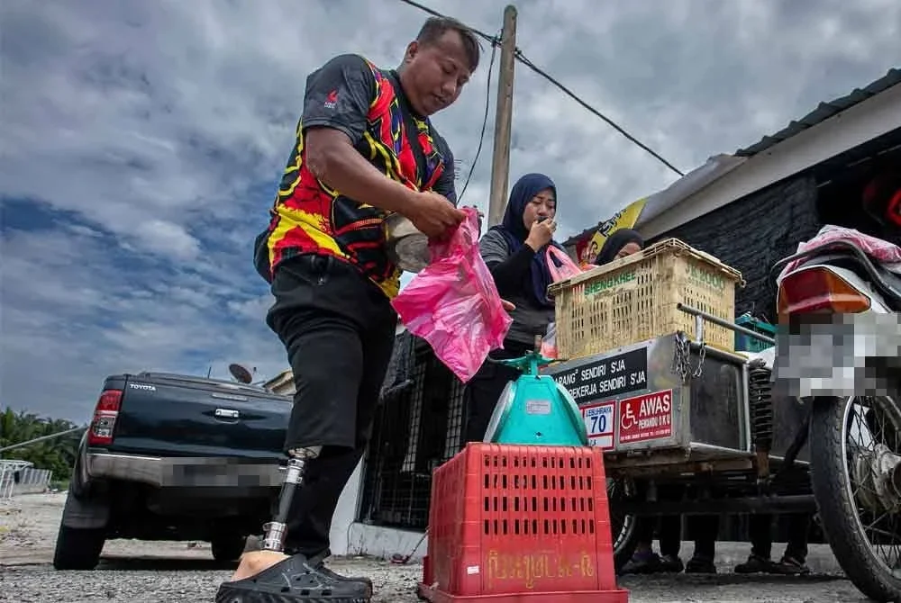 Muhammad Irwani atau dikenali sebagai 'Wan Sekerat' melayan pelanggan yang membeli buah-buahan yang dijual menggunakan motosikal roda tiganya di sekitar Bota. Foto Bernama