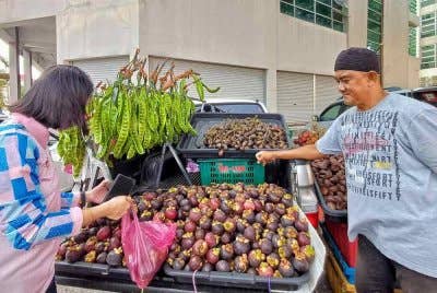 Muhammad Zaim (kanan) melayan pelanggan yang datang ke gerai buahnya di jalan pasar Kuantan pada Jumaat. Foto Sinar Harian.