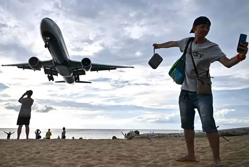 Seorang pelancong merakam swafoto ketika pesawat mendarat di Pantai Mai Khao, Phuket, Thailand. Foto AFP