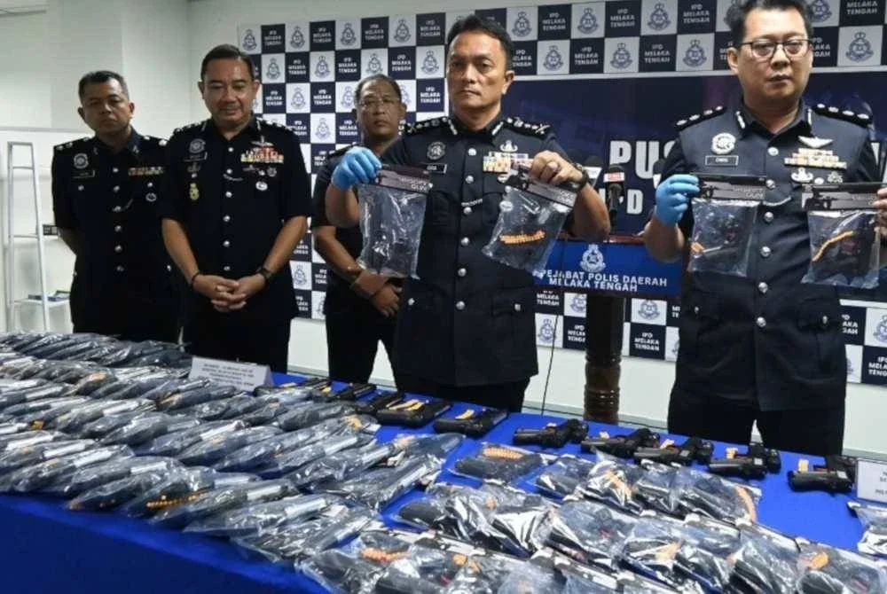 Zulkhairi (tengah) memegang pistol tiruan yang dijual tanpa lesen dan permit yang sah dari sebuah premis.