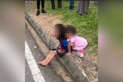 Tangkap layar video tular menunjukkan dua kanak-kanak perempuan duduk di tepi jalan.