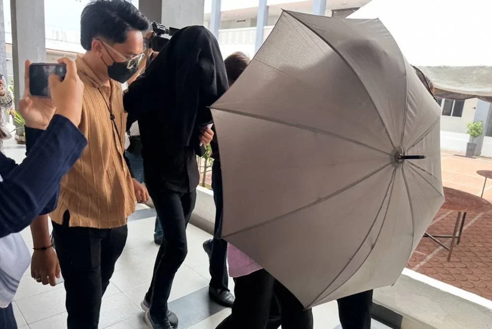 Muhammad Al Azamuddin (kanan) di sebalik payung dan Mohamad Syahmi Firas (dua dari kiri) bertutup dengan kot berwarna hitam berjalan keluar meninggalkan pekarangan Mahkamah Kota Bharu. FOTO SINAR HARIAN - ADILA SHARINNI WAHID