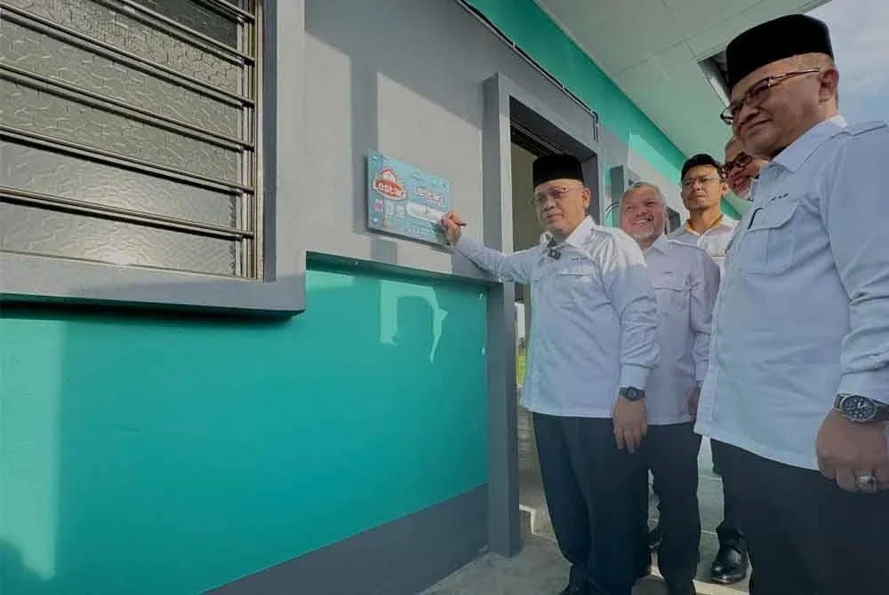 Mohd Na'im (kiri) menandatangani plak pada rumah bina baru milik Tahir di Penaga pada Rabu.