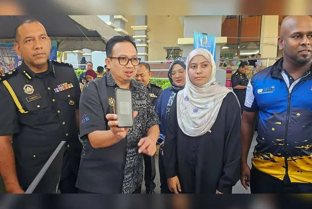 Kamalludin (dua dari kiri) menunjukkan aplikasi mobil sistem eCOSS yang boleh digunakan pengunjung bagi pembelian minyak masak peket bersubsidi di PJRM KPDN Perak di Ipoh.