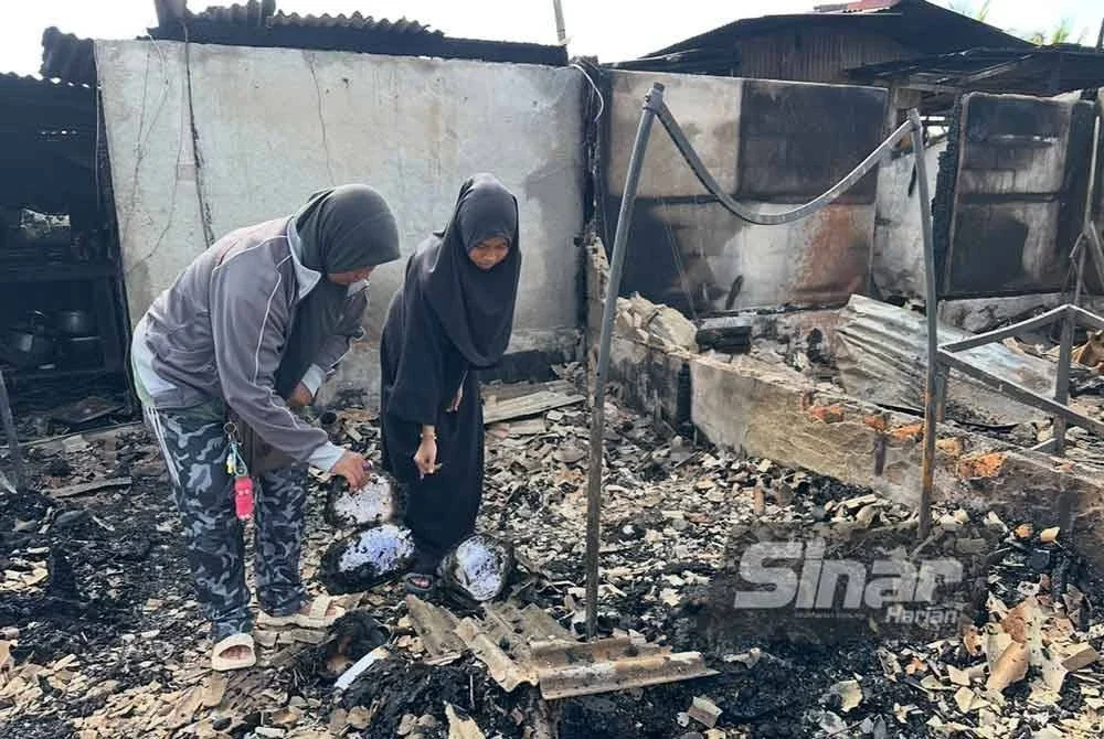 Ruzila (kiri) bersama anaknya melihat buku sekolah yang hangus. FOTO SINAR HARIAN - ADILA SHARINNI WAHID