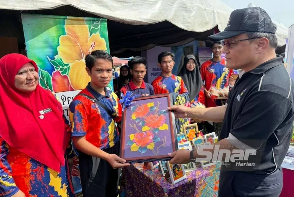 Mohd Dusuki (kanan) yang melihat dan menerima cenderamata batik hasil tangan pelajar Sekolah Menengah Kebangsaan Abdul Samad di Machang.