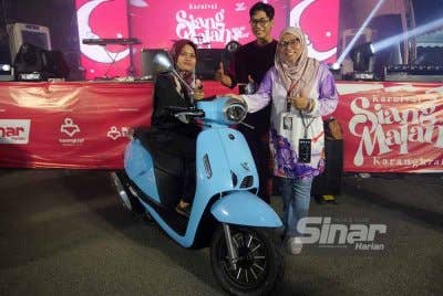 Firdaus (kanan) menyampaikan hadiah cabutan bertuah kepada Kartini sambil disaksikan Meen Tahrin (tengah) di Karnival Siang Malam Karangkraf di Shah Alam pada Ahad.