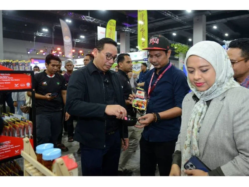 Ketua Pengarah RISDA, Zainal Azni Zulkifli (kiri) mencuba makanan yang diberikan oleh usahawan ketika melawat reruai di MITEC pada Rabu.