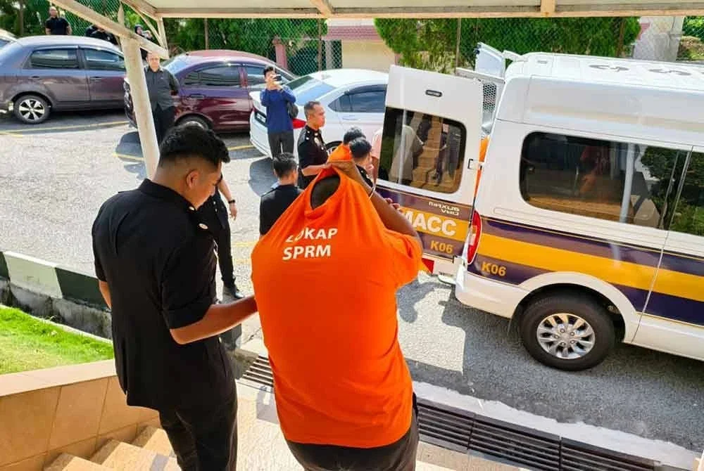 Salah seorang suspek diiringi pegawai SPRM ketika dibawa untuk perintah reman di Mahkamah Majistret Temerloh pada Khamis.