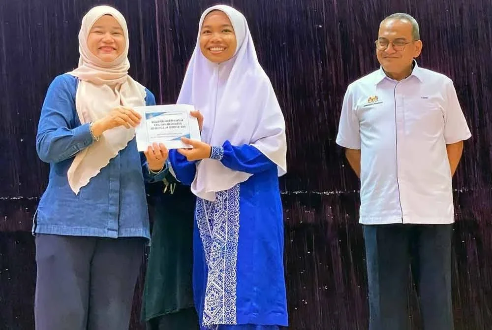 Fadhlina (kiri) menyampaikan BAP kepada salah seorang pelajar Tingkatan Enam pada satu majlis di Sektor Sumber Teknologi Pendidikan, Pengkalan Chepa di Kota Bharu pada Ahad.