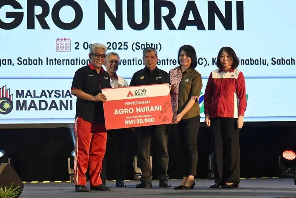 Tengku Ahmad Badli Shah (kiri) menyerahkan replika cek perlindungan takaful Agro Nurani kepada Rindah Gindol (dua dari kanan) dari Pertubuhan Pemulihan Dalam Komuniti Kota Kinabalu, disaksikan oleh Menteri Pertanian dan Keterjaminan Makanan, Datuk Seri Mohamad Sabu (tengah).