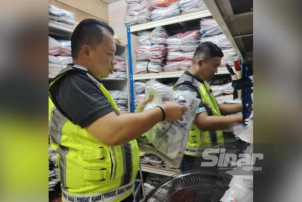 Mohd Shahran (kiri) memeriksa jersi disyaki tiruan yang ditemui dalam stor diserbu.