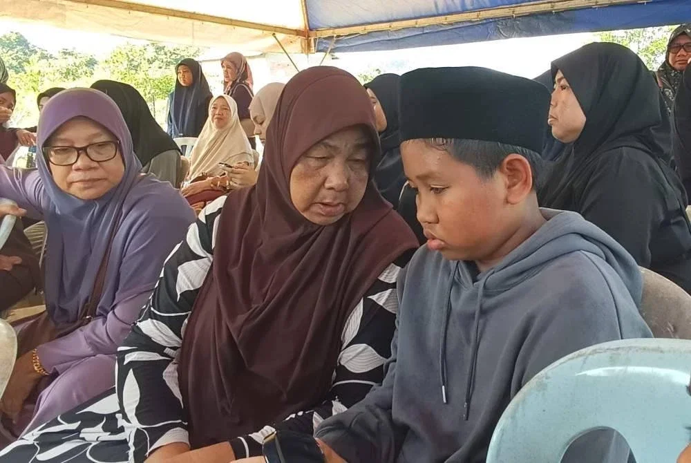 Anak sulung Allahyarham Mohd Hafizul Izham iaitu Muhammad Akif Naufal (kanan) yang sugul ditenangkan neneknya, Maznah ketika di Tanah Perkuburan Islam Kampung Pak Kancil pada Jumaat.