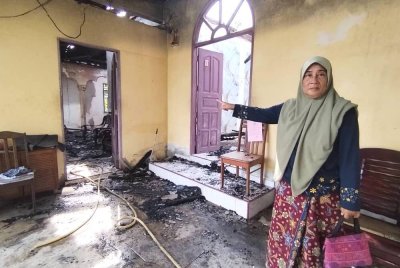 Kamariah menunjukkan rumahnya terbakar dalam kejadian awal pagi di Kampung Langkap Baru, Setiu pada Ahad.
