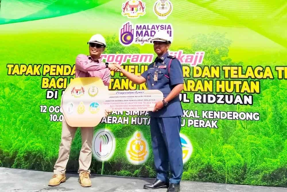 Mohamad Farhan (menyerahkan replika kunci kepada Shazlean sempena Program Ujikaji Tapak Pendaratan Helikopter dan Telaga Tiub di Hutan Simpan Kekal Kenderong, di sini pada Selasa.