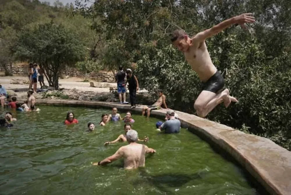 Seorang lelaki terjun ke dalam air sementara orang ramai menyejukkan badan di mata air Ein Lavan, pinggir Baitulmaqdis ketika gelombang haba melanda pada 13 Ogos 2025.-Agensi