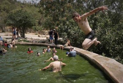 Seorang lelaki terjun ke dalam air sementara orang ramai menyejukkan badan di mata air Ein Lavan, pinggir Baitulmaqdis ketika gelombang haba melanda pada 13 Ogos 2025.-Agensi