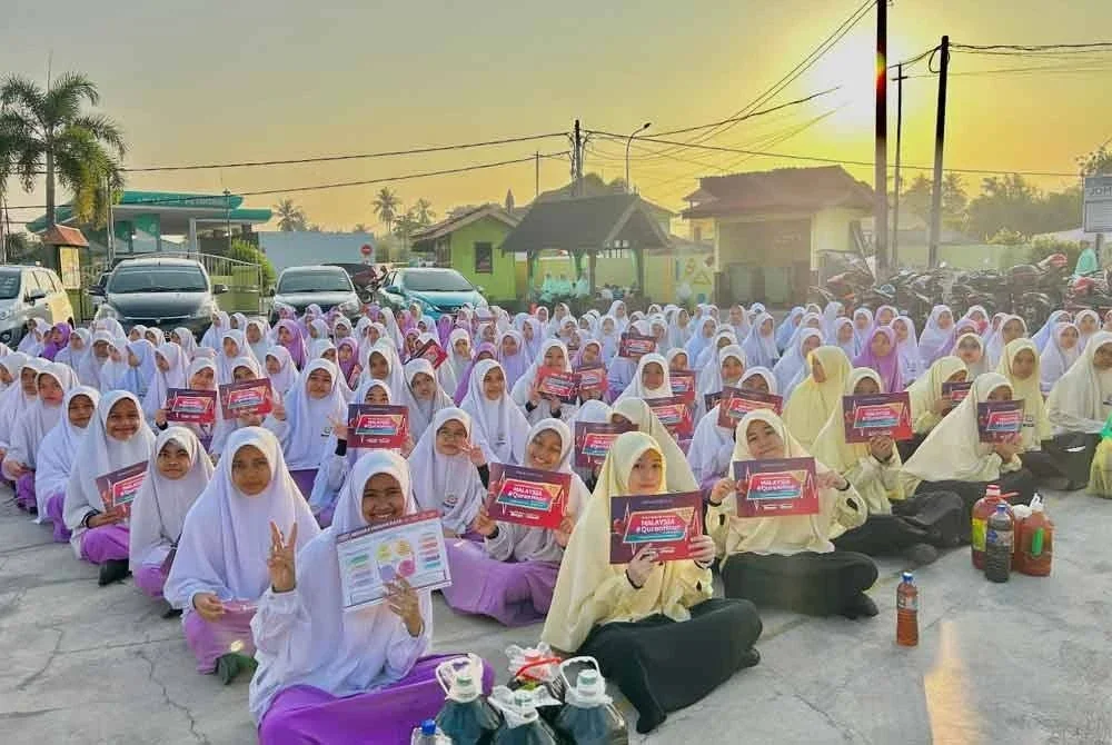 Pelajar yang berkumpul ketika perhimpunan pagi menunjukkan risalah Malaysia #QuranHour 2025.