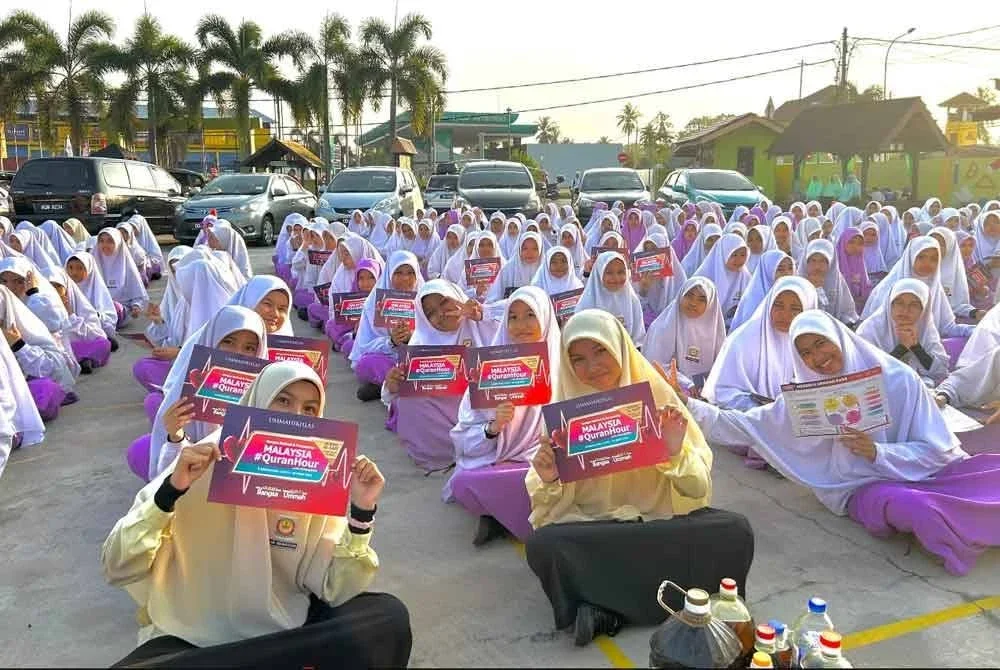 Pelajar yang berkumpul ketika perhimpunan pagi menunjukkan risalah Malaysia #QuranHour 2025.