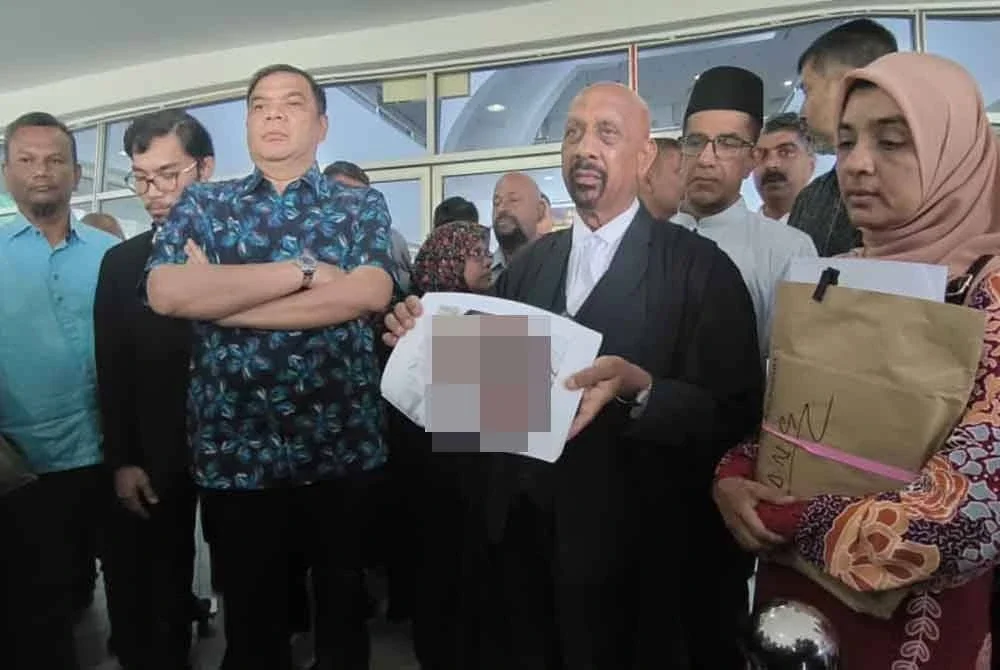 Naran Singh menunjukkan gambar Syamsul Haris yang dilampirkan dalam notis usul, dengan ditemani Ummu Haiman Bee dan ahli keluarga Allahyarham, di Mahkamah Tinggi Shah Alam pada Selasa.