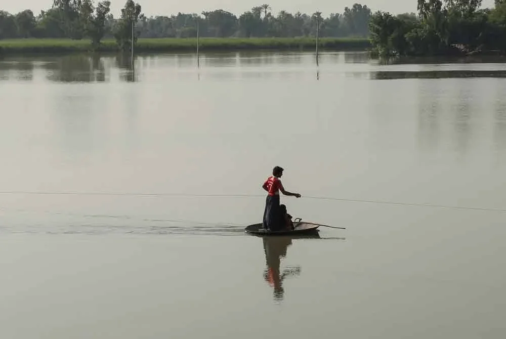 Penduduk kampung menggunakan kawah besar sambil menarik tali untuk menyeberangi kawasan banjir selepas hujan lebat di Kampung Ehsan Pur, daerah Kot Addu. Foto: AFP