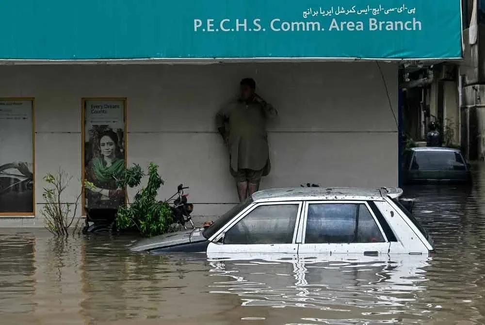 Seorang lelaki berlindung, sementara sebuah kereta kelihatan separa tenggelam dalam banjir di sebuah jalan selepas hujan lebat melanda Karachi. Foto: AFP