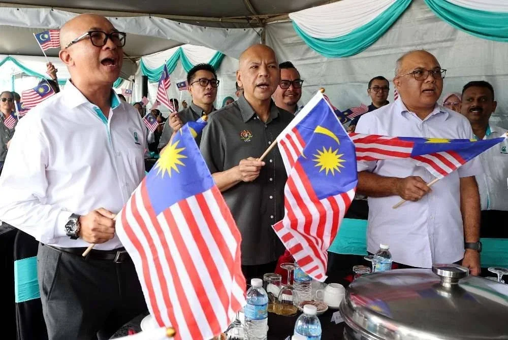 Armizan (depan, tengah) mengibarkan Jalur Gemilang bersama kakitangan Stesen Minyak Petronas Papar pada majlis penyerahan Kit Jalur Gemilang dan pelancaran Kempen Love Local di Stesen Minyak Petronas Papar hari ini. Foto Bernama
