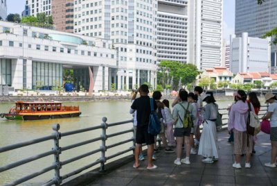 Orang ramai berjalan di tepi sungai berhampiran kawasan pusat kewangan di Singapura. -AFP