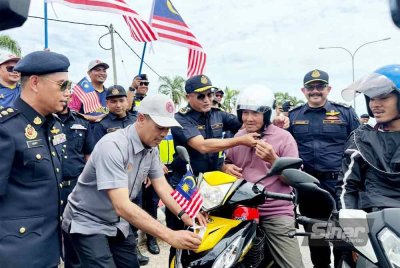 Jazmanie (empat dari kanan) memakaikan topi keledar baharu kepada penunggang motosikal.