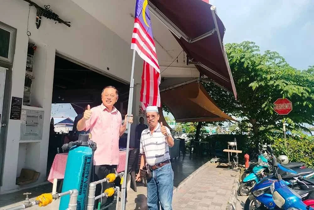 Eng Meng (kiri) mengibarkan Jalur Gemilang di sebuah restoran di Pekan Nanas pada Selasa.