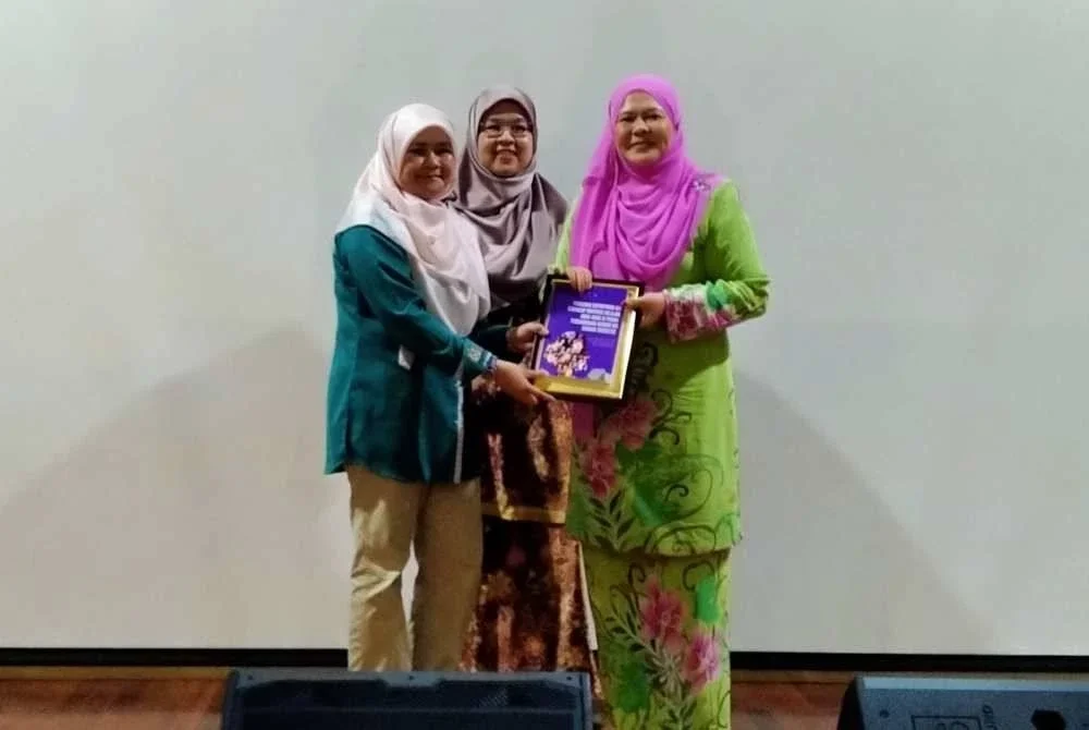 Aziah (kiri) menyerahkan buku hasil Kajian Pengaruh Kepimpinan Ibu Terhadap Motivasi Belajar Anak-anak di Perak: Penghargaan Kendiri Ibu Sebagai Mediator kepada Salbiah selepas membentangkannya di Kompleks Kementerian Dalam Negeri di Ipoh pada Selasa.