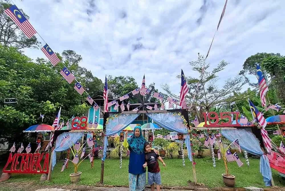 Rokiah bersama cucunya, Nur Alisha Mariam Darul Iman, 3, menunjukkan hiasan di halaman rumah mereka.