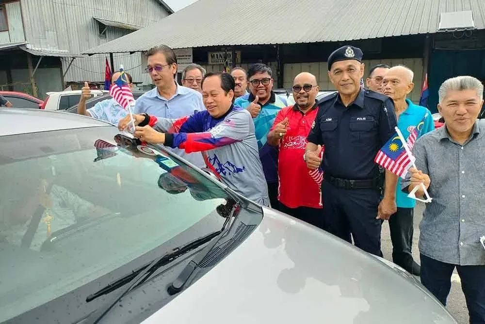 Ahmad (tengah) memasang Jalur Gemilang pada sebuah kenderaan di Pekan Kayu Ara Pasong, Pontian pada Sabtu.