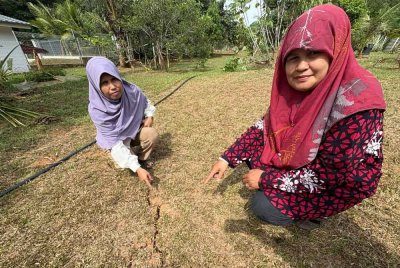 Ramlah (kiri) bersama kakaknya, Umi Kalsom Ishak, 58, menunjukkan kesan rekahan tanah ketara di kawasan kebun di bahagian belakang rumah yang dipercayai berpunca daripada gegaran gempa bumi. Foto Bernama