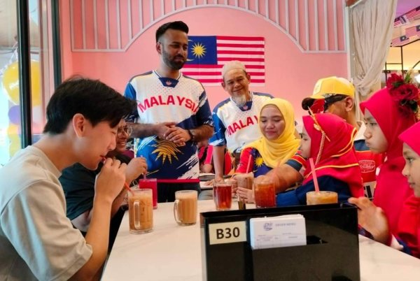 Mohd Nasmir (berdiri kiri) menghidangkan minuman percuma kepada pelanggannya di Restoran Nasi Kandar Nasmir Batu Kawan pada Ahad.