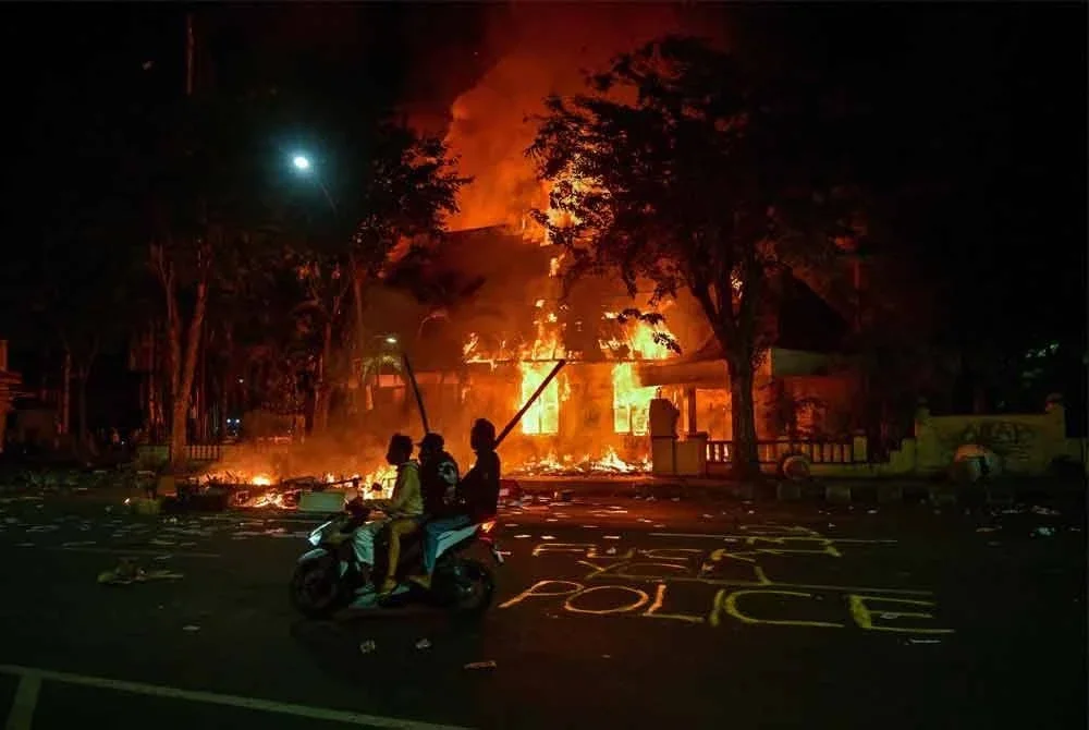 Penunjuk perasaan menunggang motosikal di hadapan ibu pejabat polis yang dibakar dan dirompak semasa demonstrasi di Surabaya. Foto AFP