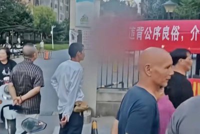 Seorang wanita bertindak menggantung sepanduk dakwa suami curang dengan rakan baik. - Agensi