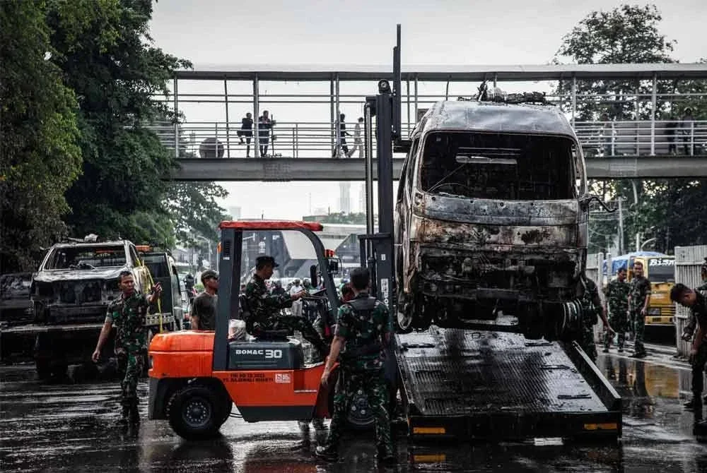 Anggota tentera Indonesia memuatkan kenderaan polis yang terbakar ke atas sebuah treler di Pejabat Pusat Peranginan Polis Jakarta Timur di Jakarta.