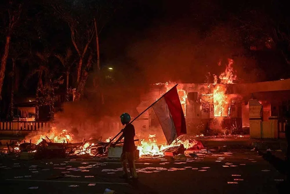 Seorang penunjuk perasaan berjalan sambil membawa bendera Indonesia di hadapan ibu pejabat polis yang dibakar dan dirompak ketika demonstrasi di Surabaya pada Ahad lalu. Foto AFP