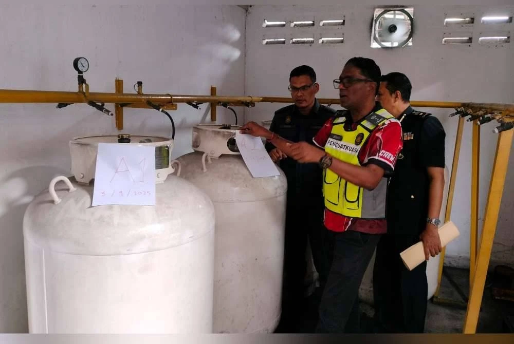 Jegan (tengah) bersama pegawai kanan KPDN Pulau Pinang memeriksa sebahagian tong LPG yang ditemui di kilang terbabit pada Rabu.