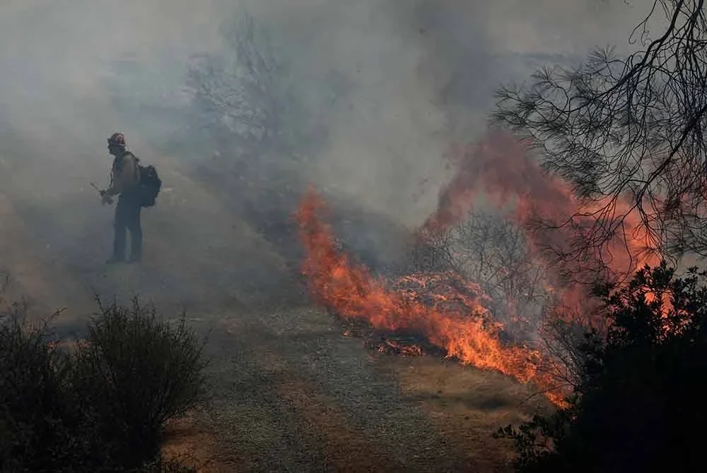 Seorang anggota bomba daripada Cal Fire berjalan berhampiran kepulan api, yang merupakan sebahagian daripada siri kebakaran hutan Kompleks September Lightning TCU, di Chinese Camp, California pada 3 September 2025.