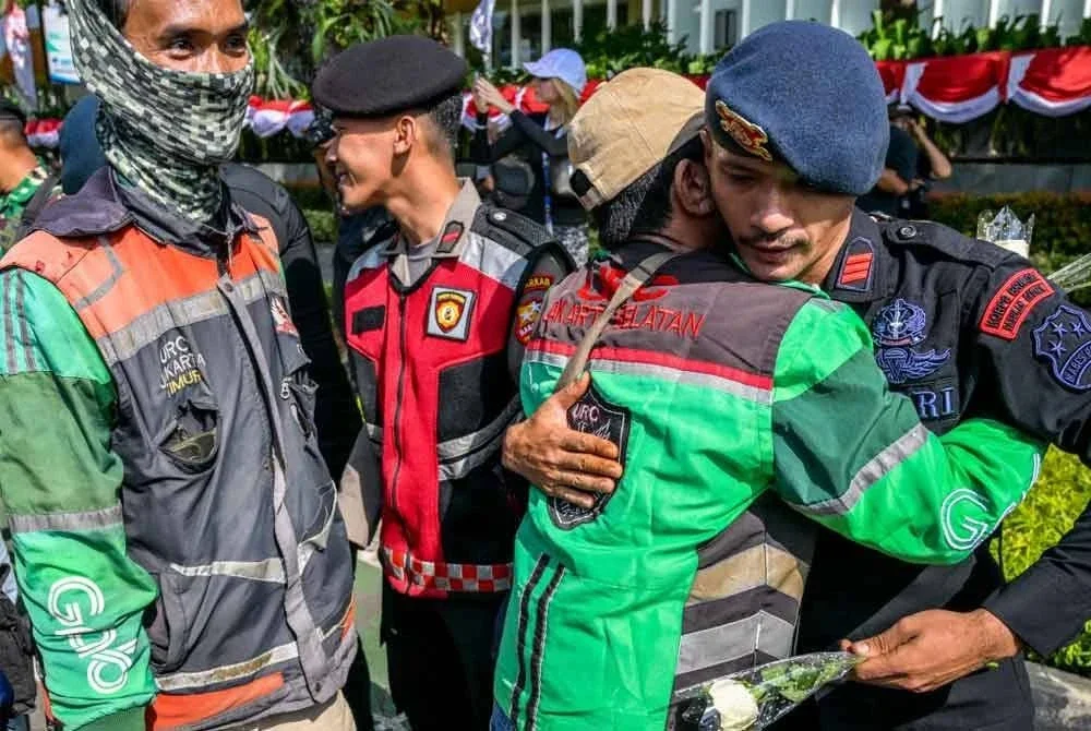 Seorang pemandu ojol dan anggota polis berpelukan ketika himpunan aman di Jakarta. - AFP