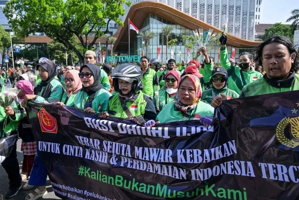 Pemandu ojol berarak membawa kain rentang bertulis mesej damai ketika himpunan bersama polis di Jakarta. - AFP