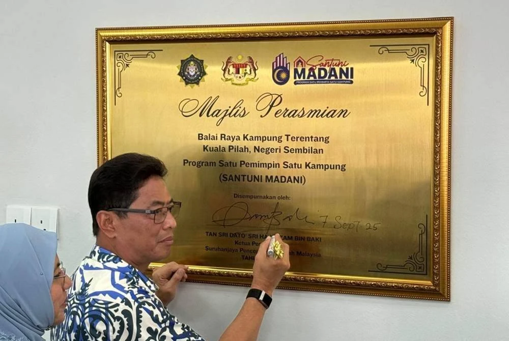 Azam menurunkan tandatangan pada plak sempena perasmian balai raya Kampung Terentang di Kuala Pilah pada Ahad.
