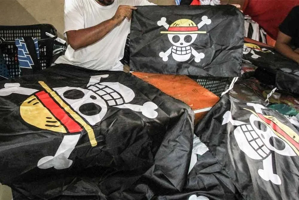 Seorang pekerja memegang bendera lanun dari anime Jepun One Piece untuk dijual di Karanganyar, Jawa Tengah. Foto: Agensi