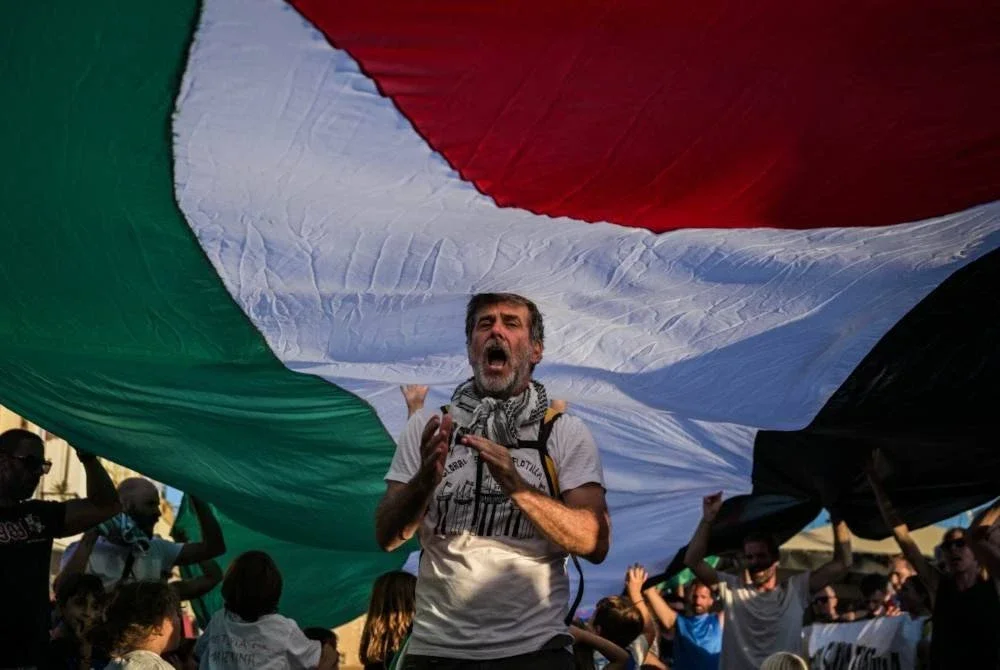 Seorang lelaki berdiri di bawah bendera Palestin gergasi di Pelabuhan Pulau Spyros bagi menyokong kapal flotila ke Gaza. AFP