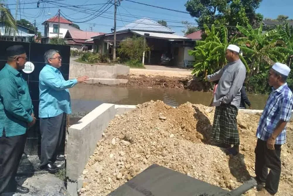 Rashidi (dua dari kiri) bersama beberapa penduduk kampung meninjau kerja-kerja menggantikan titi lama yang memerangkap sampah ketika banjir.