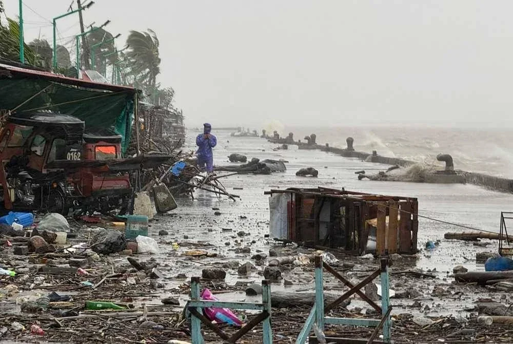 Seorang lelaki berdiri berhampiran timbunan runtuhan di jalan tepi laut di bandar Aparri, wilayah Cagayan, Filipina.