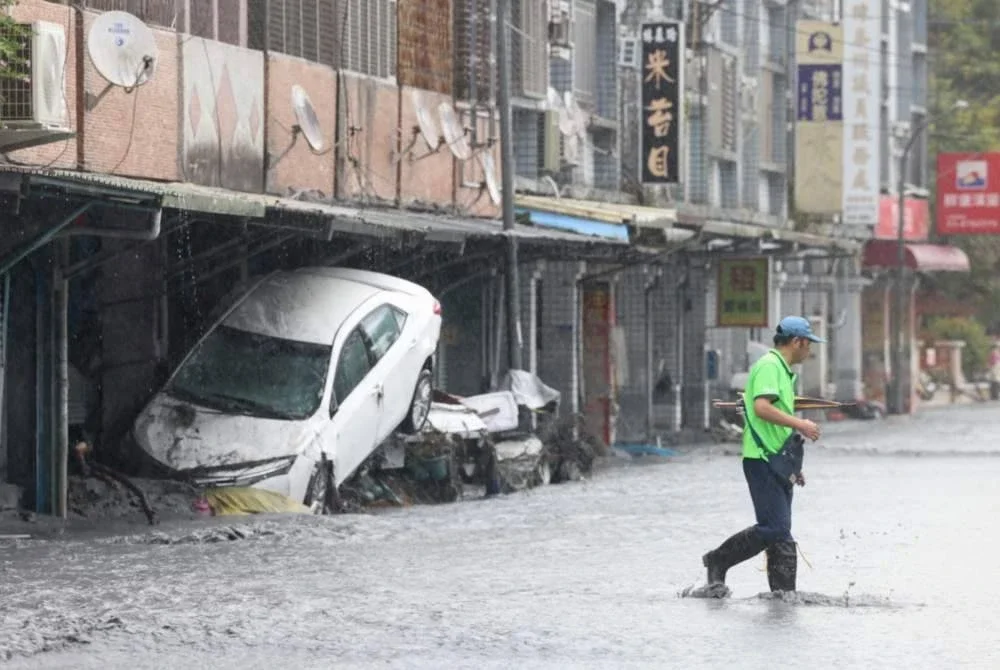 Seorang lelaki berjalan melepasi kereta rosak yang dihanyutkan banjir di Hualien, Taiwan, susulan empangan tasik pecah ketika taufan Ragasa melanda.