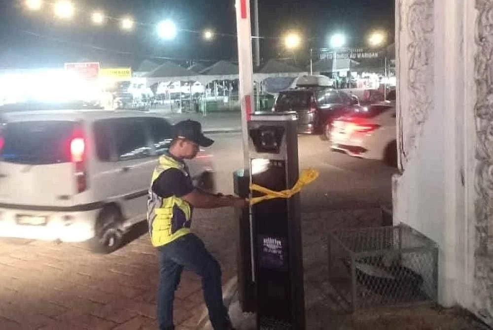 Pekerja MBKT menampal notis pada palang parkir yang dipasang tanpa kebenaran di pintu masuk dan keluar Pulau Warisan di Kuala Terengganu. Foto MBKT
